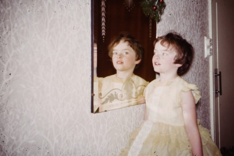 Image of young girl in a yellow dress looking sideways n a mirror
