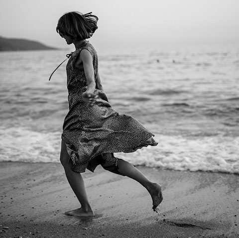Black and White Image of woman in loose dress running alone on the beach